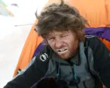 Zmęczony alpinista z białym nalotem na ustach, prawdopodobnie objawy choroby wysokościowej. W tle namioty.