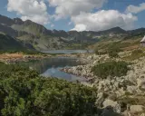 Malownicza dolina Roztoki z jeziorem i górami w tle. Drewniana chata górska na zboczu, kamieniste wybrzeże i kosodrzewina.