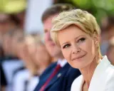 Kobieta z blond włosami w super krótkiej fryzurze damskiej, w białej marynarce, uśmiecha się.