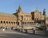 Familien genießen einen sonnigen Tag auf der Plaza de España in Sevilla. Kinder lachen, während sie über die Brücke spazieren, die über einen Kanal führt.