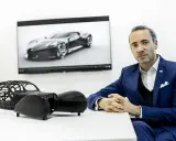 Ein Mann in einem blauen Anzug sitzt vor einem Bildschirm mit dem Bugatti La Voiture Noire. Daneben ein Modell des Autos.
