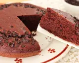 Una fetta di torta al cioccolato morbida, cosparsa di gocce di cioccolato, viene servita da una tortiera intera.