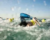 Schwimmer mit gelben Kappen kämpfen sich durch die Wellen. Die triathlon strecken sind anspruchsvoll.