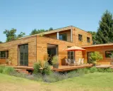 Maison moderne en bois avec terrasse et jardin. La construction maison ossature bois met en valeur le matériau naturel.