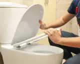 Un plombier en salopette commence à démonter la cuvette de toilette.