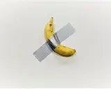 A ripe banana, a symbol of Maurizio Cattelan's art, is taped to a white wall.