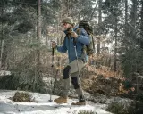 Mężczyzna w lesie z plecakiem i kijkami trekkingowymi. Dowiedz się, jak dobrać kijki trekkingowe do wzrostu, by wędrówka była komfortowa.