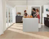 Une famille prépare un repas dans une cuisine moderne. La **délimitation sol cuisine salon** est subtile, avec un parquet clair contrastant avec le carrelage du salon.