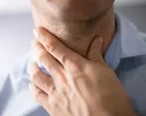 Mężczyzna trzyma się za gardło, szukając sposobów na zdarte gardło po koncercie.