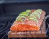 Lachs auf Zedernholz grillen, mit Limettenscheiben und Kräutern belegt. Ein saftiges Stück Fisch auf dem Rost.