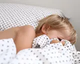 Niño rubio se esconde bajo la sábana. Aprende como hacer que un niño duerma solo con paciencia y rutinas.