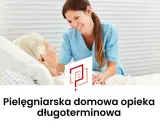Uśmiechnięta pielęgniarka środowiskowa w niebieskim uniformie pochyla się nad starszą pacjentką w łóżku. Wizyta pielęgniarki środowiskowej w domu.