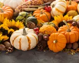 A festive autumn display featuring a variety of pumpkins, gourds, sunflowers, pinecones, acorns, and nuts.