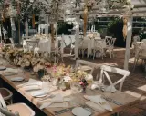 Romantische Hochzeitslocation Ideen: Ein langer Holztisch mit Blumenarrangements, Kerzen und weißen Stühlen, bereit für Gäste.