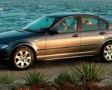 Szary sedan BMW E4 na plaży, z morzem w tle.