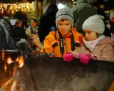 Niños disfrutan de una fogata en Italia, con luces festivas de fondo.