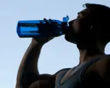 Mann trinkt aus blauer Flasche, erfrischt sich nach dem Sport.