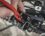 Dłoń z czerwonym narzędziem wykonuje regulację hamulca tarczowego w rowerze, przybliżając klocki do tarczy.