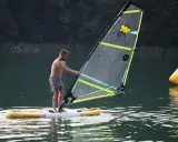 Mężczyzna na desce z żaglem, gotowy do wind sup. Na żaglu pszczółka i napis "3.5".