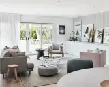 Elegante salón con sofás grises y rosas, mesa de centro y **cuadros apoyados en muebles** de la pared.