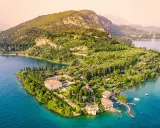 Punta San Vigilio: eine Villa mit Gärten und Zypressen am türkisfarbenen Gardasee, umgeben von grünen Hügeln.