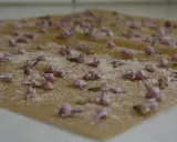 Små, lila syrenblommor strös med socker på ett bakplåtspapper. Kanderade syrenblommor som väntar på att torka.