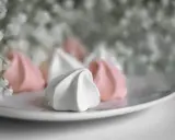 Douceur aérienne de meringue italienne rose et blanche sur une assiette, avec des petites fleurs en arrière-plan.