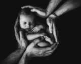 Mani adulte proteggono un neonato addormentato, simbolo di amore e cura. Un futuro di bilinguismo bambini inizia qui.