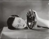Foto Man Ray: volto femminile addormentato accanto a una maschera africana tenuta da una mano.