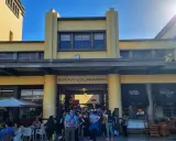 Menschen drängen sich vor dem Mercado dos Lavradores, einem gelben Gebäude mit Cafés und Geschäften.