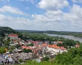 Widok na miasteczko z rzeką i lasami. W oddali widać wzgórze z krzyżami.