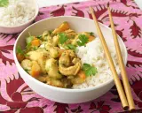 Ein köstliches Bananencurry mit Hähnchen, Karotten und Reis, garniert mit Koriander. Chopsticks liegen bereit.