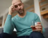 Mężczyzna z bólem głowy trzyma szklankę alkoholu, być może doświadczając reakcji disulfiramowej objawy.