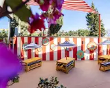 Terraza de restaurantes con zona infantil en Madrid, decorada con rayas rojas y blancas y coloridos adornos circulares. Mesas de madera con sombrillas a rayas invitan a disfrutar.