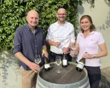 Drei Personen präsentieren Wein. Die Flasche mit Auxerrois Aussprache ist im Fokus.