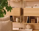 Mysig soffa med kuddar framför en hylla i ljust trä. Perfekt för dansk inredning inspiration med böcker och dekorativa föremål.
