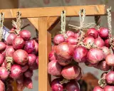 Zwiebeln trocknen: Bündel von roten Zwiebeln hängen an einem Holzgestell. Die Zwiebeln sind mit Stroh zusammengebunden und werden so gelagert.
