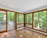 Amplio solárium con grandes ventanales y puertas de madera que dan a un porche. El color ventanas pvc de madera complementa el entorno boscoso.
