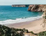 Ein einsamer Surfer genießt die Wellen am Sagres Strand, umgeben von steilen Klippen und dem weiten Atlantik.