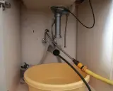 Pod zlewem żółta miska zbiera wodę, a próba udrożnienia zatkaną rurę spiralą nie pomaga.