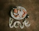 Dolce foto neonato 1 mese dorme in una cesta, circondato da fiori e dalla parola "love" creata con tessuto.