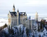 Zamek Neuschwanstein w zimowej scenerii, otoczony ośnieżonymi drzewami i krajobrazem.