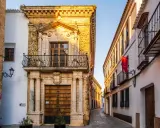 Calle empedrada flanqueada por edificios históricos, un ejemplo de los pueblos bonitos de Sevilla. Fachada de piedra dorada con balcón y puerta de madera.