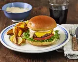En saftig hamburgare med ost, sallad och tomat, serverad med klyftpotatis och en skål med hemlagad hamburgerdressing.