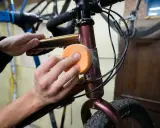 Hände polieren den Fahrradrahmen mit einem orangen Schwamm, um den Fahrradlack auszubessern.