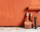 Deux pinceaux et un rouleau à peinture, prêts à rattraper trace de rouleau peinture sur un mur orange texturé.