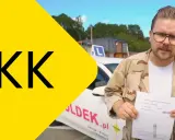 Mężczyzna w okularach trzyma dokument z napisem "Numer PKK". W tle biały samochód z literą L.
