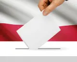Dłoń wrzuca kartę do urny wyborczej na tle flagi Polski. To symbol ważnych wyborów do parlamentu.
