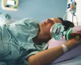Kobieta w szpitalnym łóżku, z maską gazu rozweselającego przy twarzy, przygotowuje się do porodu.