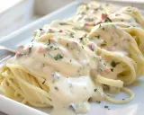 Cremige Spaghetti Carbonara mit Sahne, Speckwürfeln und Petersilie auf einem weißen Teller.
